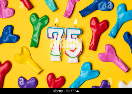 Number 75 candle with party balloons on a bright yellow background Stock Photo