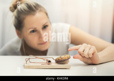 hungry woman trying to steal cookie from mouse trap. weight loss diet plan concept Stock Photo