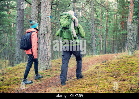 family walking forest trail with baby in child carrier on father's back Stock Photo