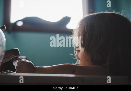 A toddler girl washing paint off her hands in a bathroom sink. Stock Photo