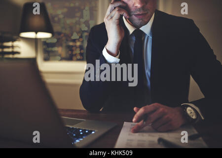 Horizontal crop shot of the accountant sitting and looking at documents while talking the smartphone. Stock Photo