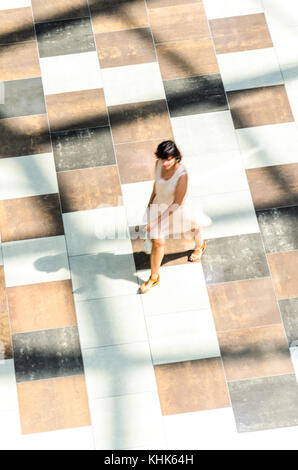 Silhouette of a Walking Brunette Woman in Bright Summer Dress, View from Above. Abstract Background of Blur in Motion Figure of a Young Woman in a Pub Stock Photo