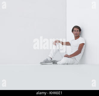 sad young man sitting beside a white wall Stock Photo