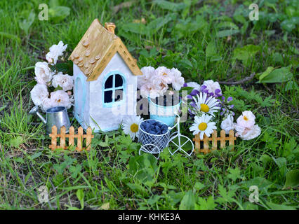 Small white house with roses and daisy flowers in the garden Stock Photo