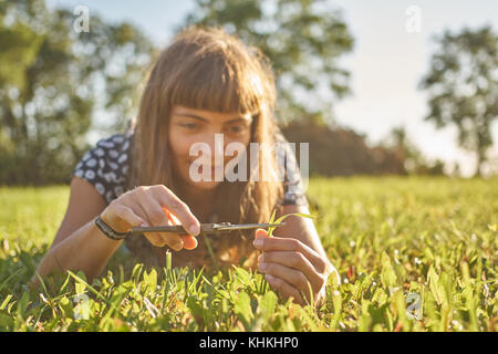 Girl cutting grass in a garden with a scissors on a sunny afternoon. Stock Photo