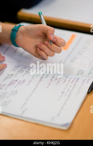 Secondary Education in the UK: close up of the hand of a pupil writing in their exercise book note books in a  maths math mathematics class lesson Stock Photo