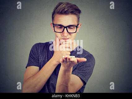 Frustrated man using a smart phone voice recognition function skeptical with search result isolated on gray background Stock Photo