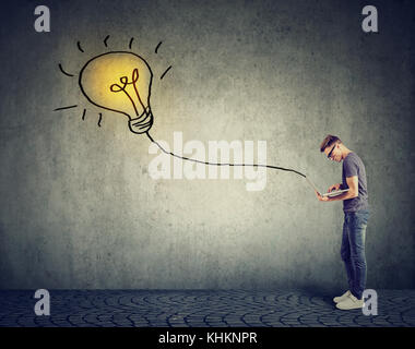 Young man using a laptop with light bulb plugged in it Stock Photo