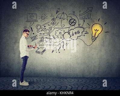 Young man using a laptop with light bulb plugged in it and info graphic plan written on concrete wall Stock Photo
