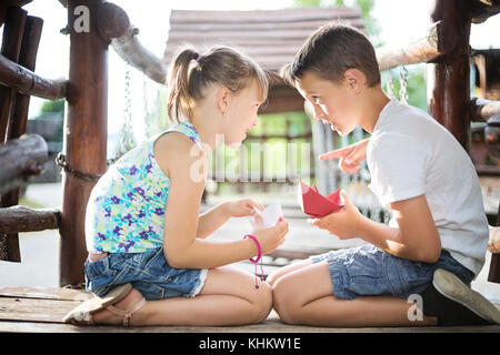 Brother and sister sitting opposite each other in a wooden house at playground, looking at each other Stock Photo