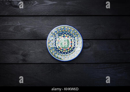 Oriental ceramic plate with beautiful colorful ornament. Top view dark wooden background. Stock Photo