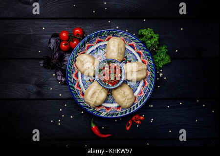 Traditional steamed dumplings Manti on plate with oriental ornament with Tomato sauce. Top view. Dark wooden background. Stock Photo