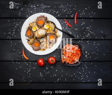 Pilaf and achichuk on white plate. Wooden dark background. Central-Asian cuisine - Plov. Top view. Stock Photo