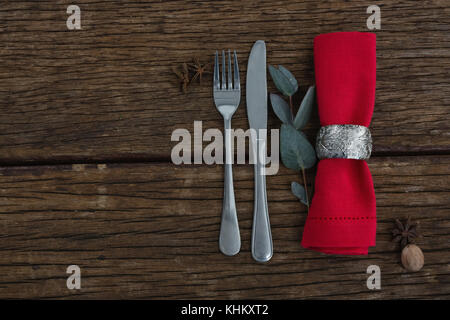 Overhead view of fork and butter knife with ingredients, leaf and napkin on wooden table Stock Photo