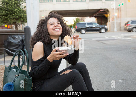 Young woman eating outside a grocery store in Queens, New York Stock Photo