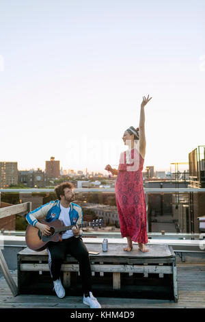 Young man playing guitar for his dancing friend Stock Photo