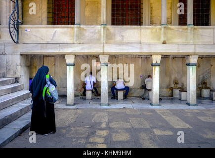 Muslim woman waits for her husband to wash his hands before entering the Blue Mosque, Istanbul, Turkey on August 19, 2015. Stock Photo