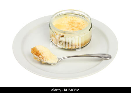 Lemon cheesecake in a ramekin with a spoon on a plate isolated against white Stock Photo