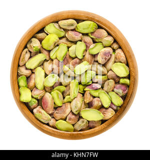 Shelled pistachio kernels in wooden bowl. Dried seeds and ripe fruits of Pistacia vera. Snack. Isolated macro food photo close up from above on white. Stock Photo