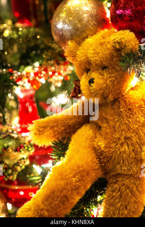 brown teddy bear in close-up against the multi-colored glittery chirstmas ball ornaments on the sparkling background of lights from behind Stock Photo