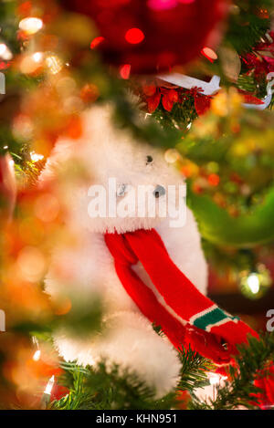 A white teddy bear with red Christmast scarf hanging on Christmast tree in focus and the foreground is the bokeh made of glittery shinning ornaments a Stock Photo