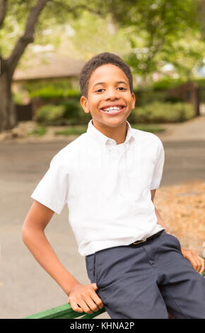 Happy Black African-American boy sitting on iron gate  in front of house in neighborhood. Space for copy in background area. Stock Photo
