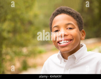 Happy African American boy smiling and looking at camera. Space for copy in out of focus trees in background area. Stock Photo