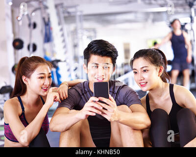 young asian man and women using mobile phone in gym while taking a break during exercising. Stock Photo