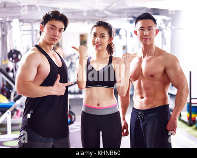 asian bodybuilders, two men and one woman, posing in gym showing muscles. Stock Photo