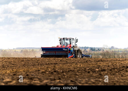 Red tractor driving on a field with a blue plow making the soil ready for the new season Stock Photo