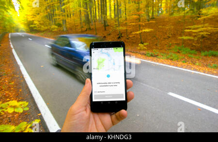Baila Tusnad, Romania, - October 15, 2017 : hand holding Smarthphone and using Uber app on road with car. Trying to get car request in rural area. Stock Photo