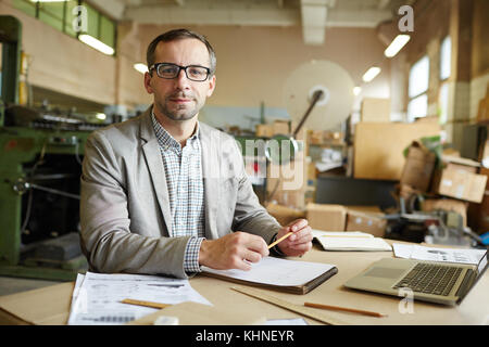 Successful middle-aged architect or industrial worker sitting by his workplace Stock Photo