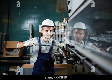 Worker in overall and harhat repairing industrial equipment Stock Photo