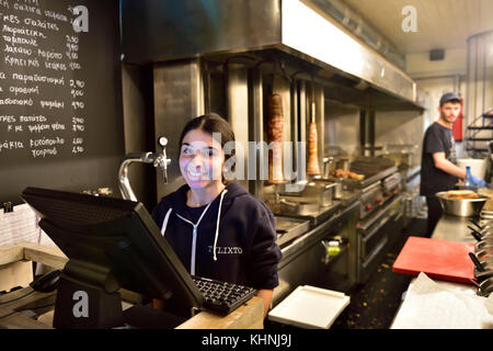 Waitress serving in Greek street food restaurant with gyros turning on spit in background, Athens, Greece. Stock Photo