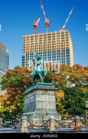 Tradition and Modernity, Past and Future in Tokyo. A modern skyscraper is under construction behind an old samurai warrior statue surrounded by autumn Stock Photo