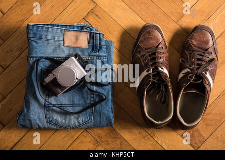 A pair of fretted blue jeans, brown shoes, and a camera lie by on the floor. Stock Photo