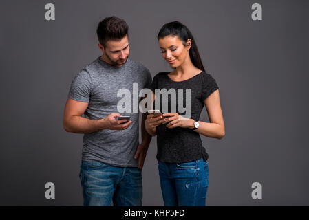 A beautiful young couple standing and showing their smartphones to each other Stock Photo