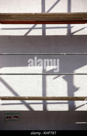 The Pipes and wooden inserts from a scaffolding cast abstract shadows on a wall. Stock Photo