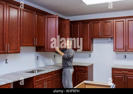 Kitchen in home worker sets a new handle on the white cabinet with a screwdriver Stock Photo