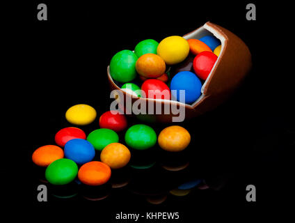 Chocolate egg with colorful small round candies on black background Stock Photo
