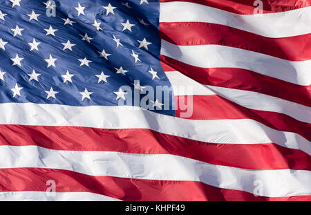 Close up of a red, white and blue American flag with stars and stripes unfurled in the wind. Photographed against a deep blue sky with cirrus clouds. Stock Photo