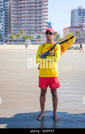 Male Brazilian firefighter lifeguard wearing a yellow shirt, red shorts, torpedo buoy standing on watch, Praia Grande Beach, state of Sao Paulo, Brazil. Stock Photo