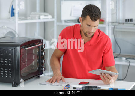 male technician checking his tablet to repair oven in kitchen Stock Photo