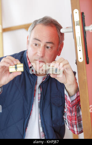 mature technician fixing lock in door in clients home Stock Photo