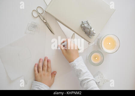 Close up photo of child´s hands holding scissors, cutting white paper, creating chrismas paper origami Stock Photo