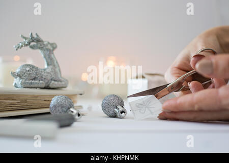 Close up photo of female hands holding a scissors, cutting a paper with hand drawn christmas present Stock Photo
