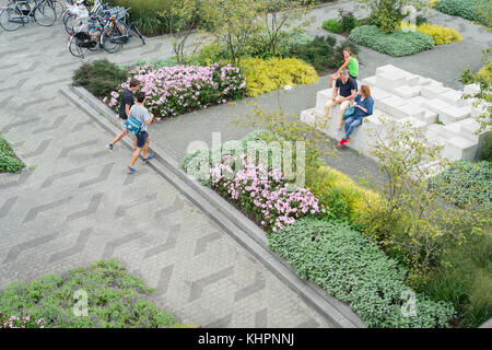 ,ROTTERDAM, HOLLAND - AUGUST 24, 2017; Three people sitting on sculptural installation and two walking through landscaped public garden with flowers,  Stock Photo