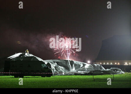 A firework explodes in the background as the remains of the Airlander 10, the world's largest aircraft, lie on the ground at Cardington airfield in Bedfordshire, after the aircraft came loose from its moorings causing its hull to rip and deflate. Stock Photo