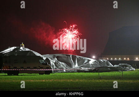 A firework explodes in the background as the remains of the Airlander 10, the world's largest aircraft, lie on the ground at Cardington airfield in Bedfordshire, after the aircraft came loose from its moorings causing its hull to rip and deflate. Stock Photo