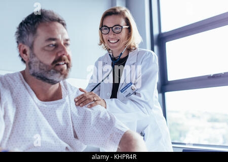 Medical examination of mature male patient in hospital ward. Woman doctor checking heartbeat of hospitalised man. Stock Photo